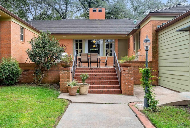 603 E Melton, Longview, TX 75602 - view of exterior entry with a chimney, brick siding, a lawn, and covered porch