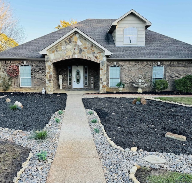 view of front of home featuring a shingled roof, stone siding, and brick siding