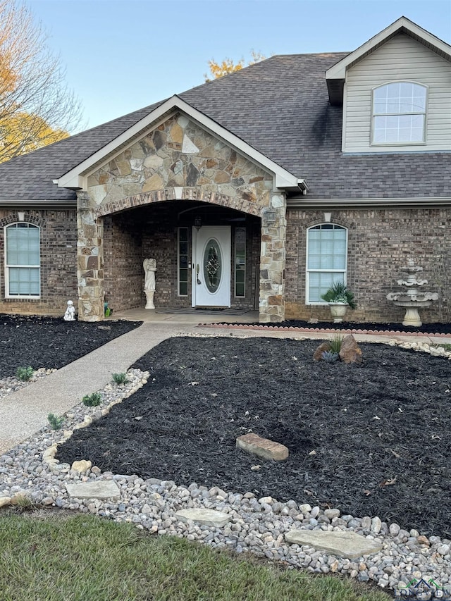 view of front facade featuring stone siding, a shingled roof, and brick siding