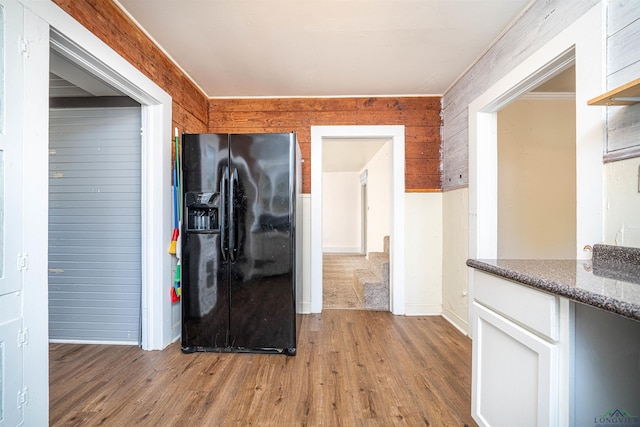 kitchen with hardwood / wood-style floors, wood walls, black refrigerator with ice dispenser, dark stone counters, and white cabinets