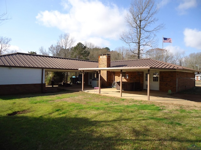 back of property featuring metal roof, brick siding, a yard, a chimney, and a patio area