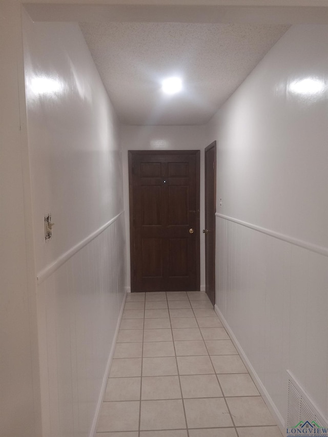 hall featuring a wainscoted wall, light tile patterned floors, visible vents, and a textured ceiling