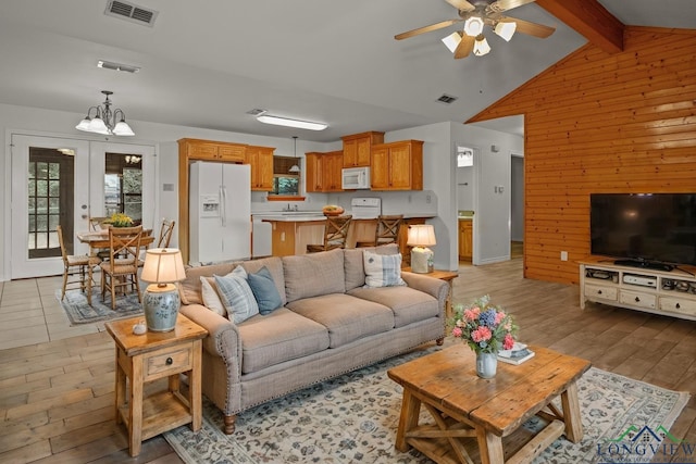 living room with lofted ceiling with beams, light hardwood / wood-style flooring, french doors, wooden walls, and ceiling fan with notable chandelier