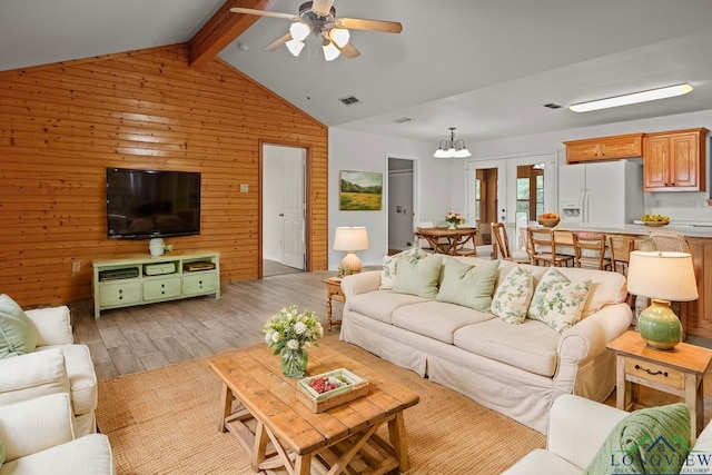 living room featuring wood walls, french doors, light hardwood / wood-style floors, ceiling fan with notable chandelier, and vaulted ceiling with beams