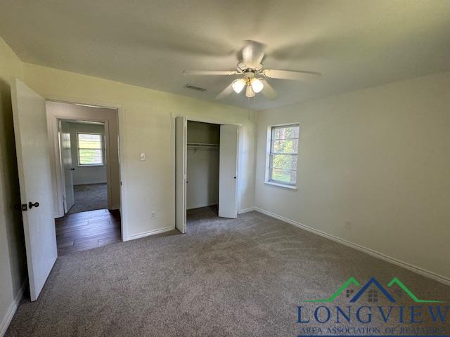 unfurnished bedroom with multiple windows, a closet, dark carpet, and ceiling fan