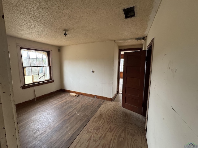 empty room featuring visible vents, a textured ceiling, baseboards, and hardwood / wood-style floors