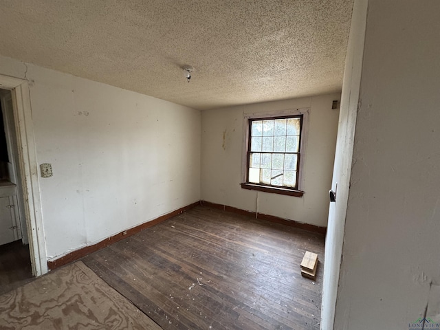 empty room with a textured ceiling, hardwood / wood-style floors, and baseboards