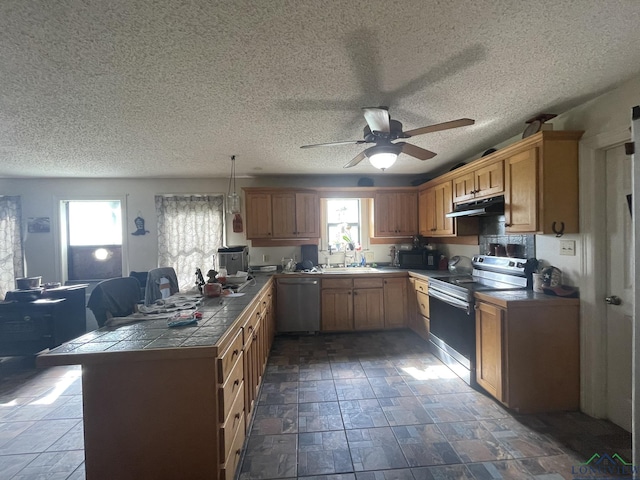 kitchen featuring ceiling fan, tile counters, stainless steel appliances, kitchen peninsula, and pendant lighting