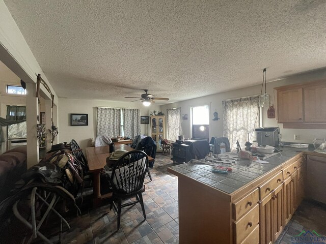 kitchen with kitchen peninsula, a textured ceiling, ceiling fan, tile counters, and hanging light fixtures