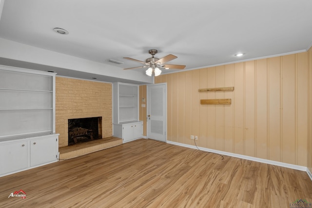 unfurnished living room with built in shelves, ceiling fan, a large fireplace, hardwood / wood-style floors, and wooden walls