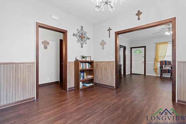 empty room featuring dark wood-style flooring, wainscoting, and ceiling fan with notable chandelier