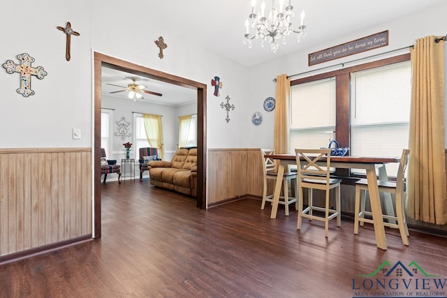 dining room featuring wood walls, ceiling fan with notable chandelier, dark wood-type flooring, and wainscoting
