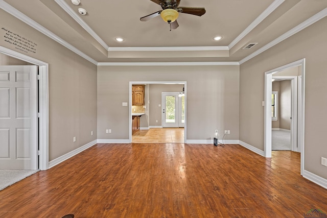 unfurnished living room featuring wood-type flooring, a raised ceiling, ceiling fan, and ornamental molding