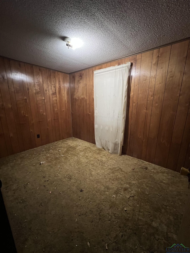 empty room with a textured ceiling and wooden walls