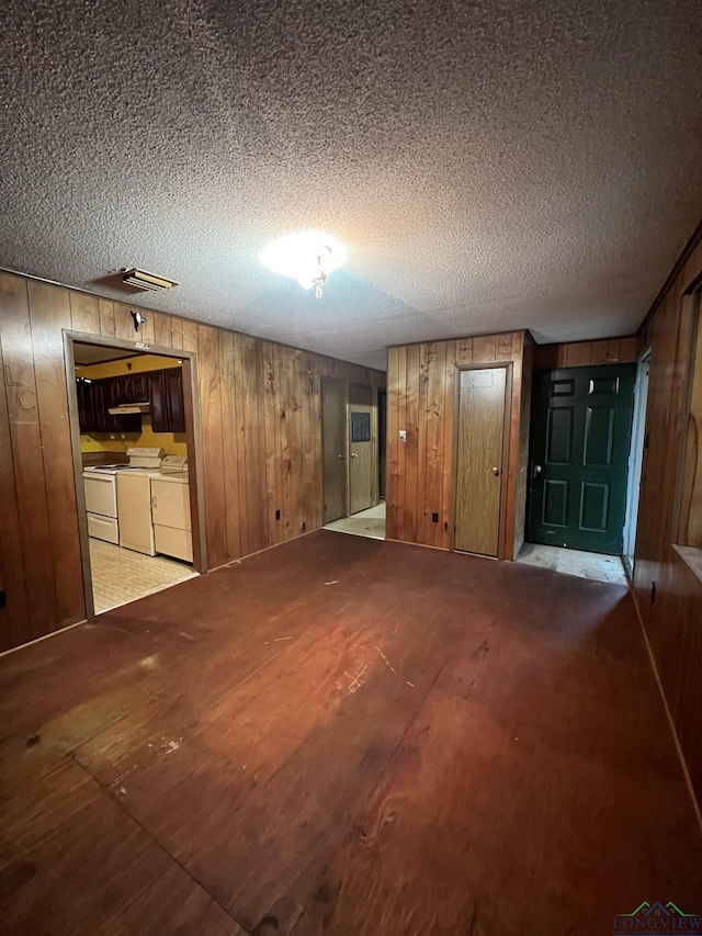 unfurnished living room featuring wood walls, independent washer and dryer, and a textured ceiling