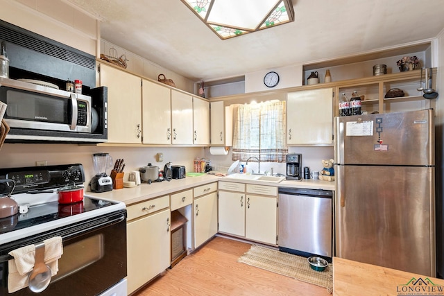 kitchen with cream cabinetry, light wood finished floors, stainless steel appliances, light countertops, and a sink