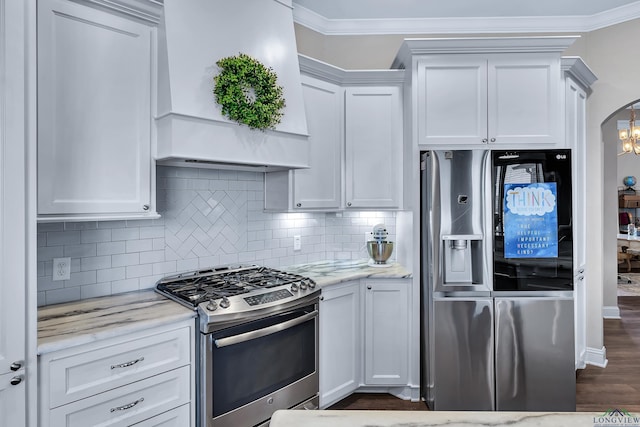 kitchen with white cabinetry, light stone counters, backsplash, premium range hood, and appliances with stainless steel finishes