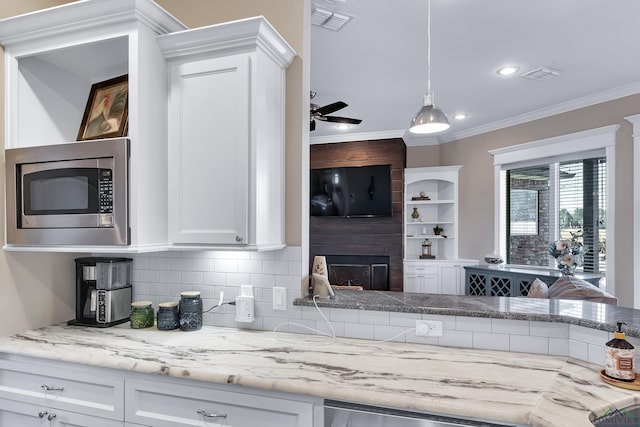 kitchen featuring decorative backsplash, ornamental molding, a fireplace, white cabinetry, and stainless steel microwave