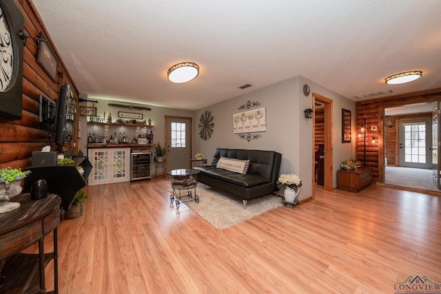 living room with light hardwood / wood-style floors, a textured ceiling, beverage cooler, and indoor bar