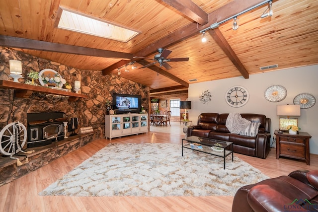 living room with wooden ceiling, a wood stove, track lighting, vaulted ceiling with skylight, and light wood-type flooring