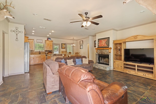 living room featuring stone tile flooring, ornamental molding, visible vents, and ceiling fan with notable chandelier