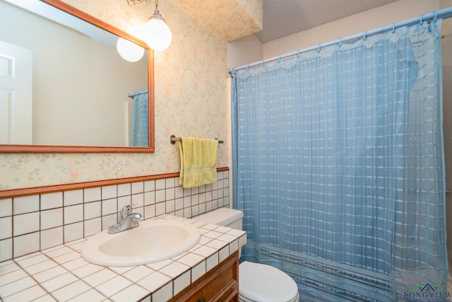 full bath featuring curtained shower, toilet, a textured ceiling, vanity, and wallpapered walls