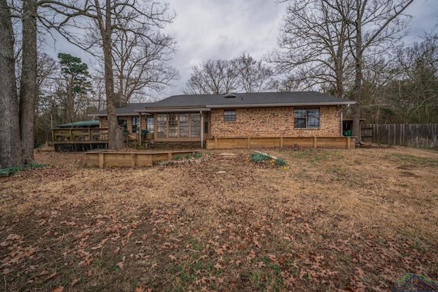 rear view of property with a deck, brick siding, fence, and a sunroom