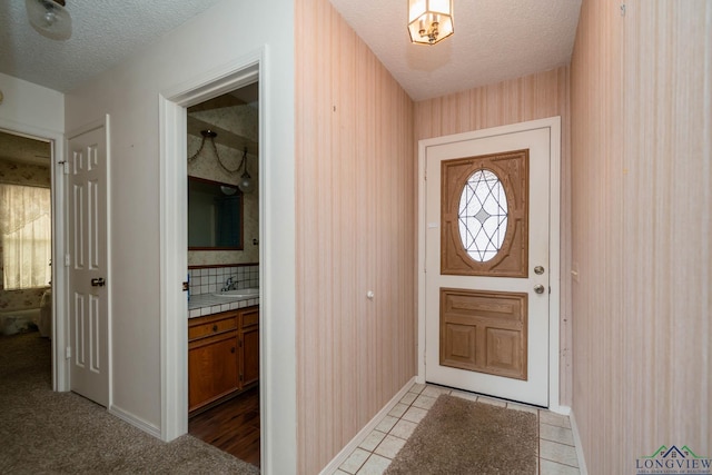 doorway to outside with light tile patterned floors, a sink, a textured ceiling, and wallpapered walls