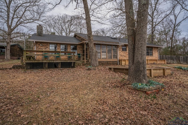 back of property with a sunroom, a chimney, fence, a deck, and brick siding