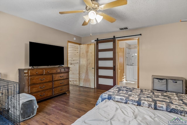 bedroom featuring a barn door, ceiling fan, dark wood-type flooring, and a textured ceiling