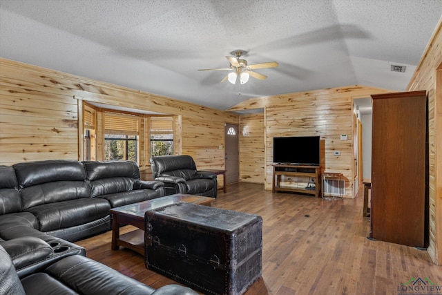 living room featuring ceiling fan, wood walls, wood-type flooring, a textured ceiling, and vaulted ceiling