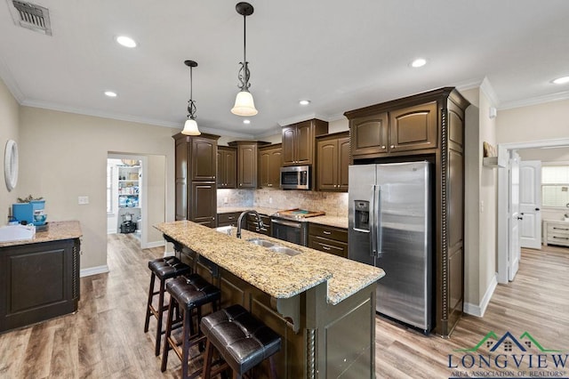 kitchen featuring dark brown cabinetry, a center island with sink, decorative backsplash, appliances with stainless steel finishes, and a sink