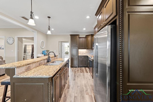 kitchen featuring a breakfast bar area, decorative light fixtures, stainless steel appliances, a sink, and a large island with sink