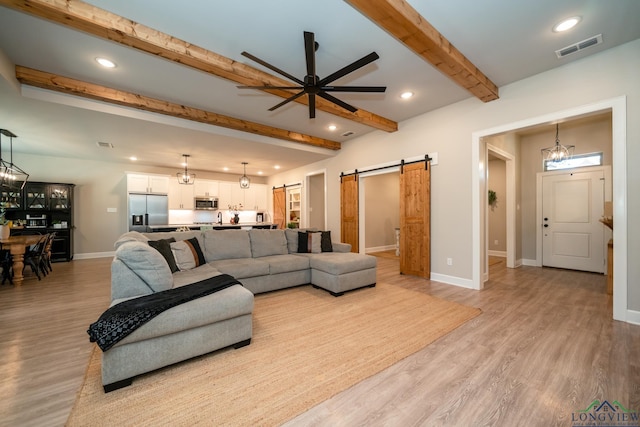 living room featuring ceiling fan, a barn door, light wood-type flooring, and beam ceiling