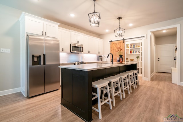 kitchen with white cabinets, a barn door, stainless steel appliances, and a kitchen island with sink