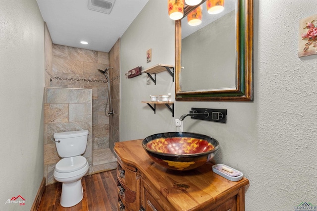 bathroom featuring hardwood / wood-style flooring, vanity, tiled shower, and toilet