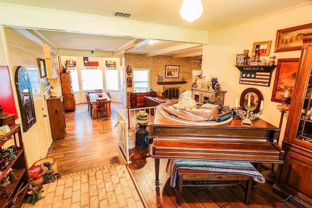 miscellaneous room with a brick fireplace, brick wall, crown molding, light hardwood / wood-style flooring, and beamed ceiling