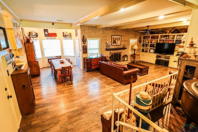 living room featuring a brick fireplace, brick wall, ceiling fan, beam ceiling, and light hardwood / wood-style flooring