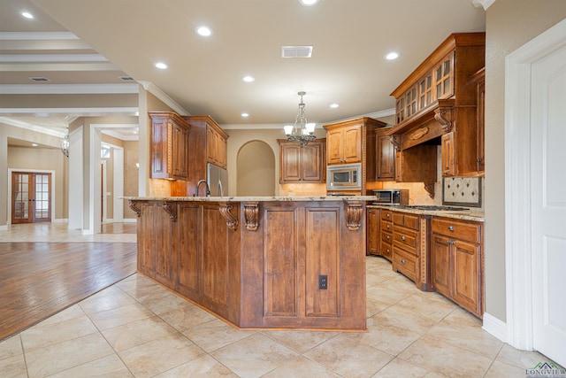 kitchen with light stone countertops, stainless steel appliances, a peninsula, brown cabinets, and a kitchen bar