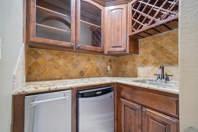 kitchen with decorative backsplash, dishwasher, glass insert cabinets, light stone countertops, and a sink