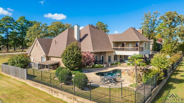 back of house with a fenced backyard, a balcony, a yard, a chimney, and a patio area