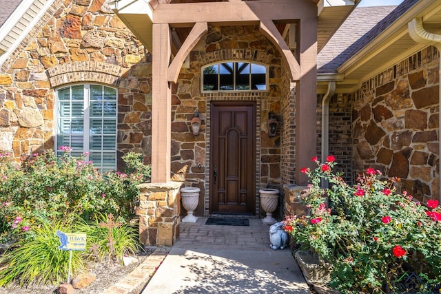 property entrance featuring a shingled roof, stone siding, and brick siding