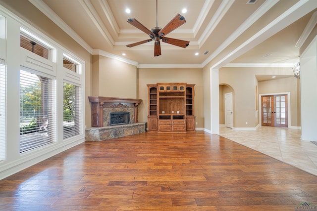 unfurnished living room with light wood-type flooring, arched walkways, ornamental molding, and a high end fireplace