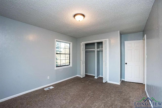 unfurnished bedroom with a closet, a textured ceiling, visible vents, baseboards, and dark colored carpet