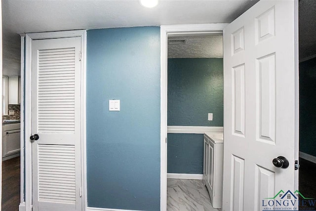 hall featuring a textured ceiling, marble finish floor, baseboards, visible vents, and a textured wall
