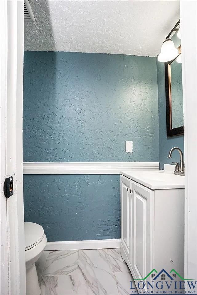 bathroom with marble finish floor, toilet, and a textured wall