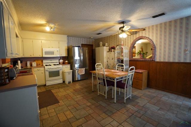 kitchen featuring white appliances, ceiling fan, a textured ceiling, white cabinets, and wood walls