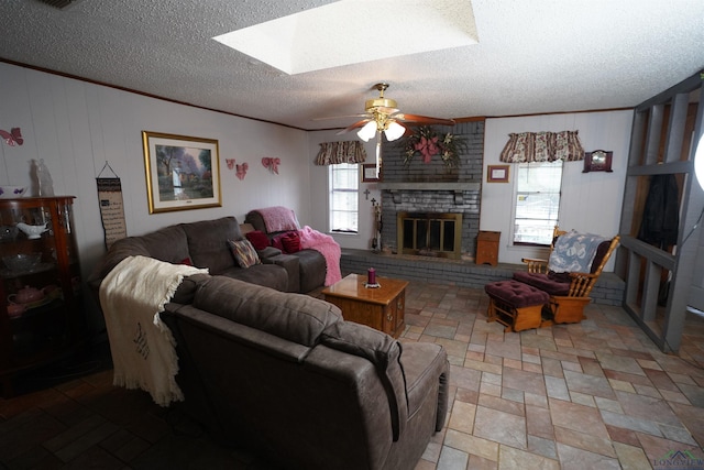 living room with ceiling fan, a brick fireplace, a textured ceiling, and a skylight