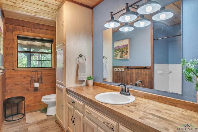 bathroom featuring wooden ceiling, toilet, wooden walls, vanity, and wood finished floors