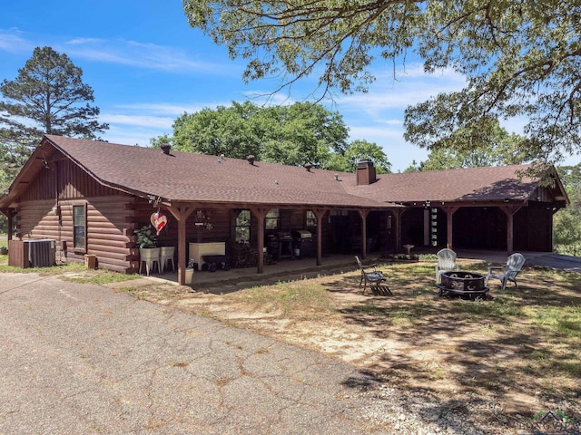 view of front facade with central air condition unit, a patio, a fire pit, log exterior, and a chimney